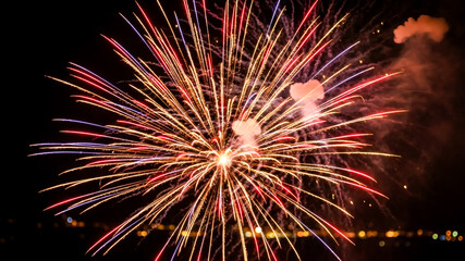 Obraz premium Vibrant red and gold firework burst with smoke against black sky. Abstract radial light trails and sparks for festive party invitation or event flyer.