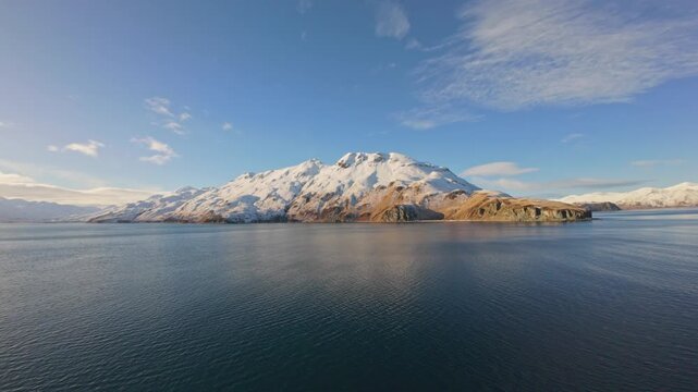 Sunny Winter Aerial View of Remote Snow-Covered Mountain and Ocean Coastline of Unalaska Island. Clear sky, cold ocean waters, and dramatic terrain of Dutch Harbor, Alaska. 