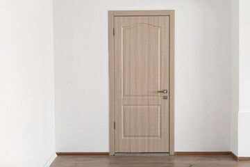 A closed wooden door stands against a white wall in a new apartment. This front entrance showcases a modern design and provides a sense of security and safety in residential living.