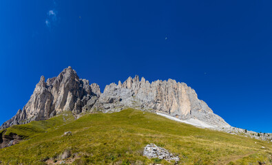 Panoramic Dolomites mountain landscape with jagged limestone peaks, alpine meadows, rocky ridges, dramatic geology, Italian Alps scenery, high altitude terrain, clear sky, natural environment