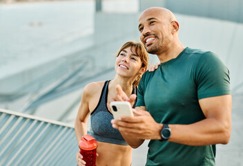 Smiling active young couple jogging exercising and having fun and laughing together taking a breakand using a mobile phone after walking and running in the park, fitness and healhty living concept