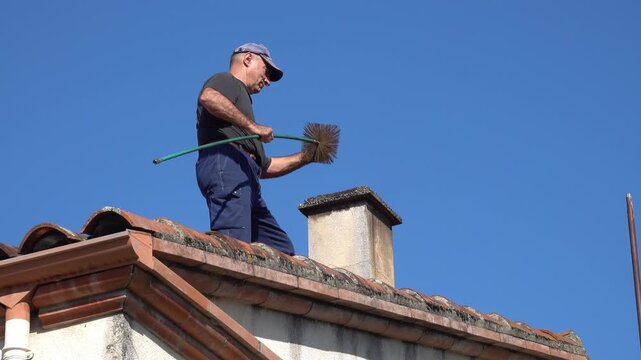 The man on the roof removes part of the brush for cleaning the fireplace chimney and continues cleaning the chimney