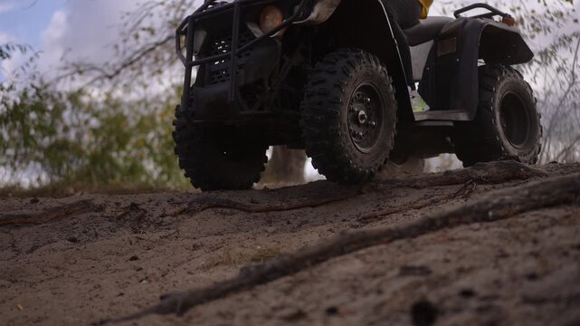 Slow motion. Female rider on quad sandy trail wearing yellow jacket navigating rough slope low angle wheel shots dusty forest backdrop closeup tire action