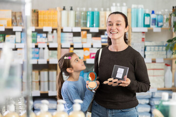 Woman with schoolgirl daughter are busy choosing dry rouge at pharmacy, compare with other good....