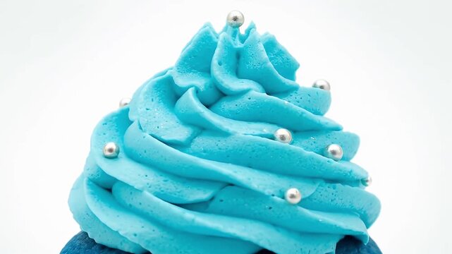 A vibrant close-up captures a beautifully crafted cupcake, featuring a rich, deep blue cake base crowned with a generous swirl of light blue frosting. Delicate silver spherical sprinkles are artfully 