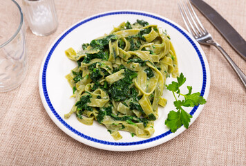Delicious al dente pasta cooked with spinach and spice sauce on a white plate, top view