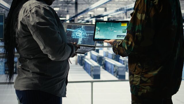 Close up of army general and coworker in data center integrating AI into radar systems for missile tracking. Teamworking soldier and technician in server hub analyzing aerial movement on device