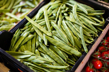 Fresh green string bean in a box on the counter of a stall. Vegetables and beans are on a shelf in a supermarket