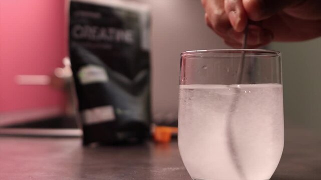 Close up of person stirring creatine monohydrate powder into a glass of water to prepare a pre workout drink for muscle strength, fitness, and athletic performance enhancement