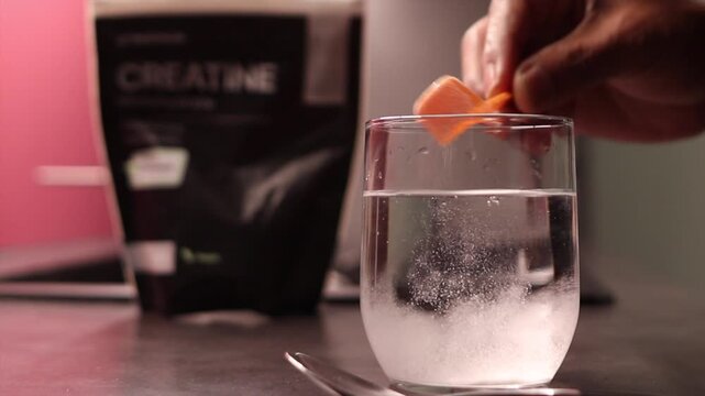 Close up of a hand scooping creatine monohydrate powder into a glass of water, stirring it with a spoon, preparing to boost muscle gain and energy before a workout