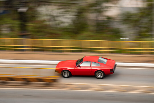 Red VW SP2 driving fast on road, Classic Brazilian sports car side panning view