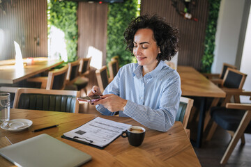 Businesswoman using smart phone working remotely from cafe