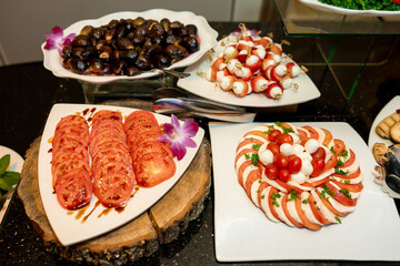 Assorted fresh appetizers including sliced tomatoes with balsamic, caprese salad with mozzarella and cherry tomatoes, stuffed mushrooms, and mozzarella-strawberry skewers on a buffet table