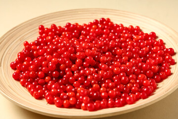 Wooden plate with fresh viburnum berries on beige background, closeup