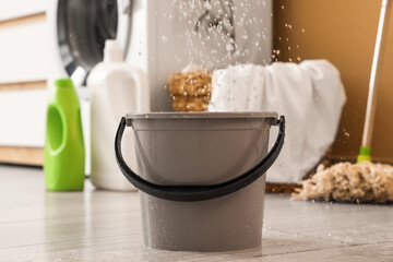 Water dripping from ceiling into plastic bucket on floor in laundry room