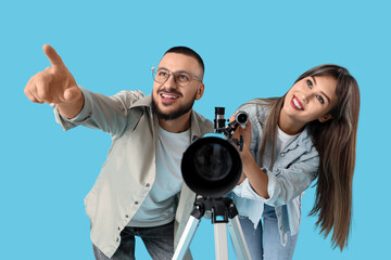 Fototapeta premium Young couple with telescope pointing at something on blue background