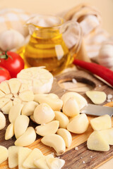 Wooden board with fresh garlic cloves and jug of oil on beige background, closeup