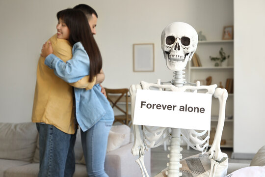 Human skeleton model with text FOREVER ALONE against young couple hugging at home