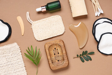 Reusable cotton pads with bag, gua sha massage tool, soap bar and bottle of cosmetic on brown background