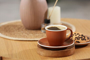 Cup of hot coffee and plate with tasty cookies on wooden table in room