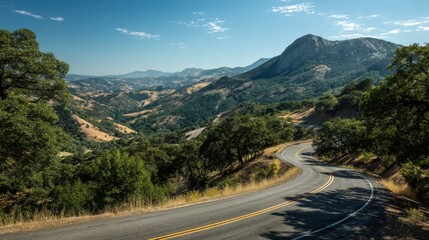 Fototapeta premium A winding road with trees on both sides and a mountain in the background. The road is empty and the sky is clear