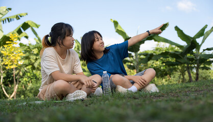 Two girls relaxing on grass outdoors, chatting after playing badminton.