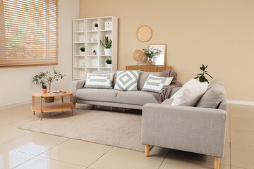 Interior of living room with comfortable sofa, coffee table, shelving unit and houseplant