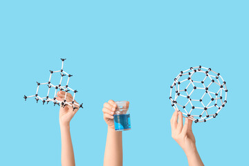 Female hands holding bottle with liquid and molecular models on blue background. Chemistry lesson concept