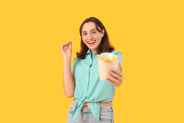 Beautiful young woman with french fries on yellow background