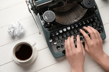 Woman typing on typewriter with cup of coffee and crumpled paper on white wooden background