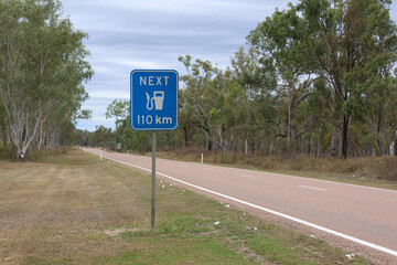 Roadside sign warning the next petrol gas fuel station is 110km away in a rural Australian area with eucalyptus trees © Tammy Walker
