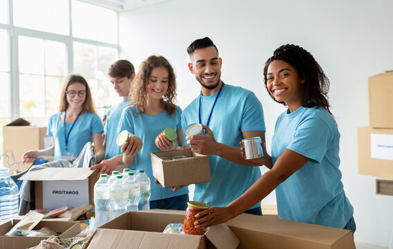 A diverse group of volunteers smiles while sorting donated food at a community charity donation center. They prepare boxes filled with essentials for those in need.