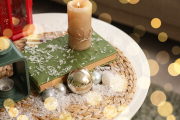 Book with candle, Christmas balls and snow on table in room, closeup