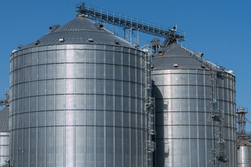 Two large silo tanks are in the background. The tanks are silver and have a reflective surface