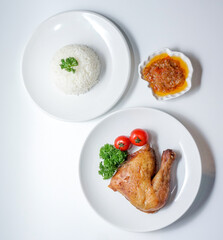 Top view of roasted chicken leg served with steamed white rice, chili sauce, and garnish on white plates. Clean flat lay food image with copy space, ideal for Asian cuisine, menu, or lifestyle content
