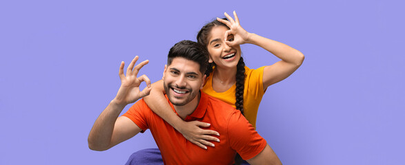 Two young adults express joy while playfully posing together. They are smiling and making hand gestures, showcasing their friendship and happiness in a vibrant setting.