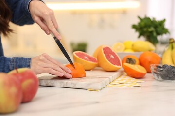 Woman cutting fruits for blending at white marble table indoors, closeup