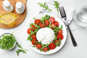 Delicious burrata cheese with arugula and tomatoes served on light table, flat lay