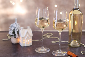 Glasses of white wine and Christmas decor on grey table against background with blurred lights
