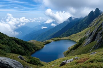 A deep blue mountain lake sits nestled among green hillsides with cloudy mountain peaks in the background