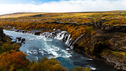 Aerial view of stunning Hraunfossar waterfalls in Iceland during summer. Turquoise glacial water cascades over ancient lava fields creating a unique natural wonder