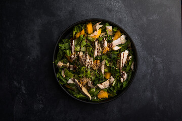 Fresh lettuce salad with roasted turkey and mango served on a dark black background