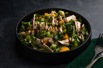 Fresh lettuce salad with roasted turkey and mango served on a dark black background