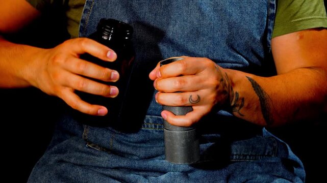 Extreme close up of male barista hands with tattoos pouring coffee beans and grinding with manual grinder. Detailed view of forearm muscle tension and grip in dark studio.