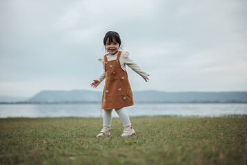 happy toddle girl palying and dancing on grass field near the river
