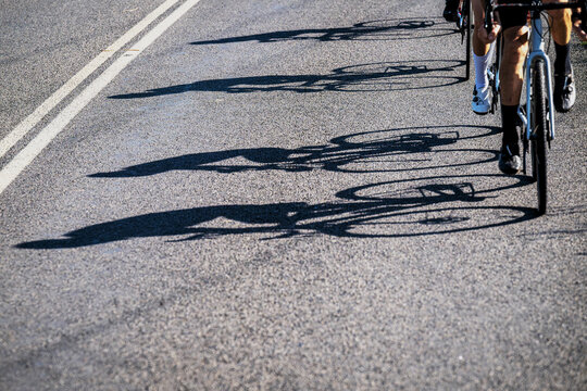 A road showing the shadows of a line of pushbike riders and their cycles - horizontal