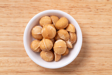 Peeled macadamia nuts in a bowl on wooden background, Table top view