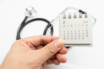 Hand holding desk calendar set to FEBRUARY 2026. Doctor Appointment Schedule and Annual Health Checkup Reminder. Preventive medicine, healthcare planning, doctor visits, and timely examinations.