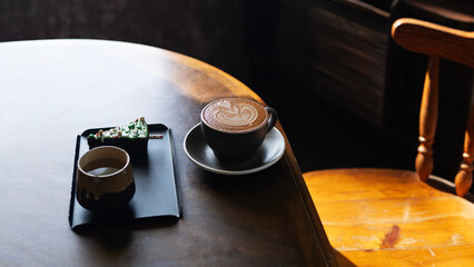Mocha coffee and warm water and slice of cake on wooden table under warm sunlight