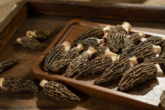 Close up of dried morel mushrooms, a gourmet culinary ingredient, on a wooden plate with a dark rustic background